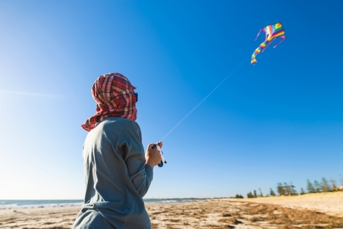 Boy launching his colourful kite high in the sky from the beach - Australian Stock Image
