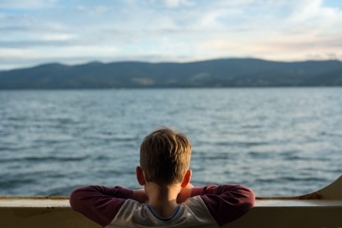 Boy looking above railling on ferry at the ocean