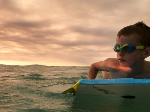 Boy on a bodyboard in the ocean at sunset - Australian Stock Image