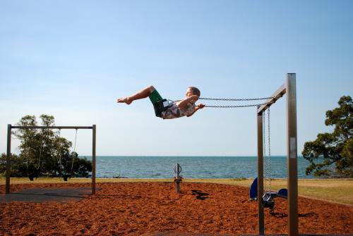 Boy on a swing in a playground near the sea - Australian Stock Image