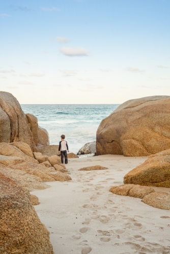 Boy on sandy beach surrounded by boulder rocks - Australian Stock Image