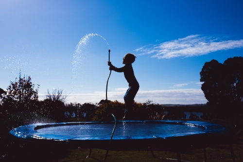 boy on trampoline with garden hose