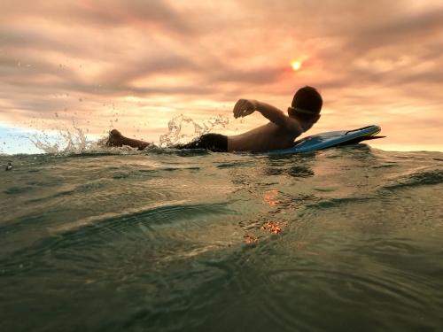 Boy paddling on his body board at sunset