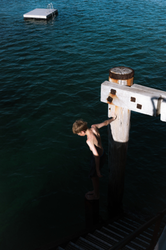 Boy preparing to jump from Jetty into ocean in late summer sun - Australian Stock Image