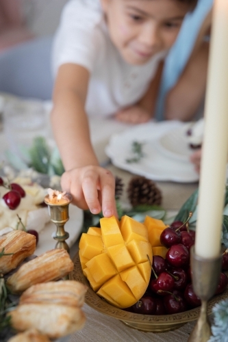 Boy reaching to grab slice of mango from bowl - Australian Stock Image