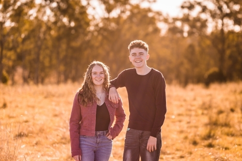 Boy resting arm on girl's shoulder happy in afternoon glow from sun - Australian Stock Image