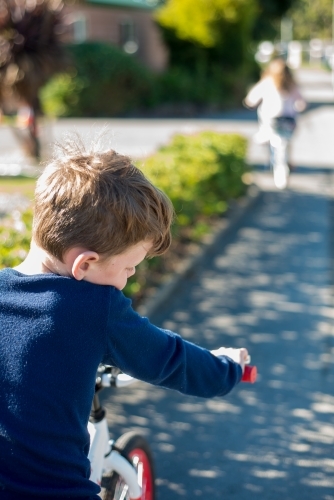 Boy riding a bike following girl on road - Australian Stock Image