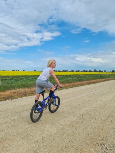 Boy riding bike down country lane beside canola field - Australian Stock Image