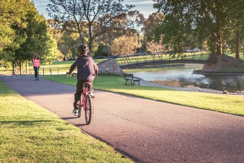 Boy riding his bicycle along the bike lane in Adelaide Park Lands on a day - Australian Stock Image