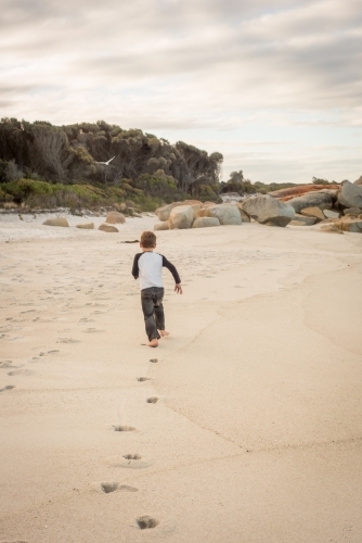 Boy running along beach leaving footprints
