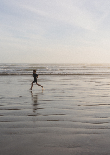 Boy running along remote beach at sunset - Australian Stock Image