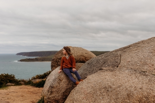 Boy sitting on large rock with ocean behind