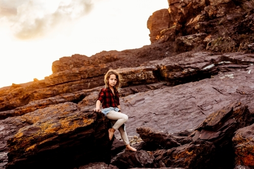 Boy sitting on rocks at sunset - Australian Stock Image