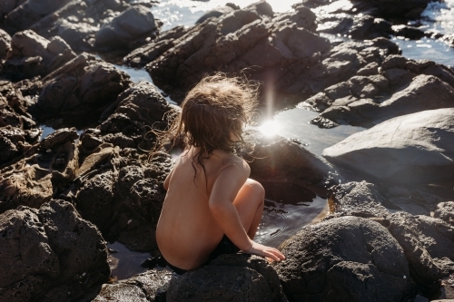 Boy sitting on rocks next to the ocean - Australian Stock Image