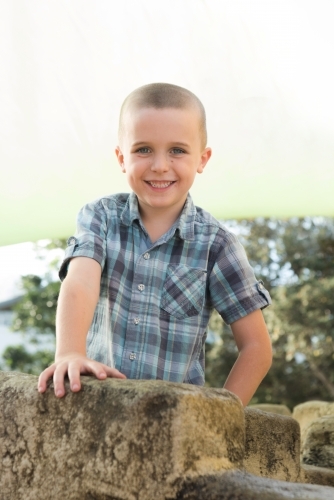 Boy standing behind rock smiling at camera. - Australian Stock Image
