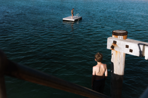 Boy standing on jetty watching girl on pontoon In the distance - Australian Stock Image
