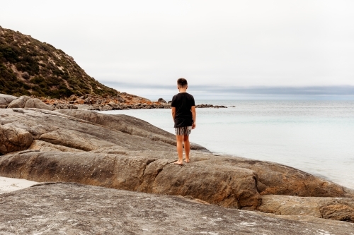 Boy standing on rocks looking at the ocean