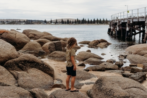 Boy standing on rocks next to the ocean and jetty