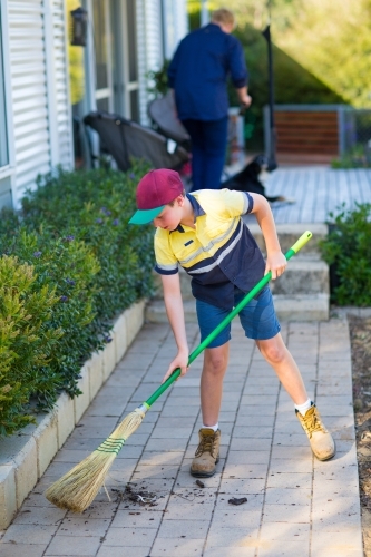 Boy sweeping path with raw broom - Australian Stock Image