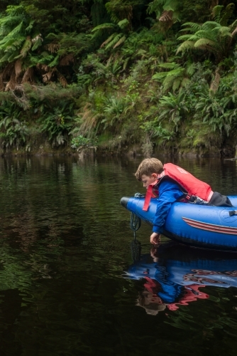 Boy trailing his hand in river water from a kayak