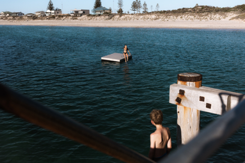 Boy waiting to jump off jetty while watching girl in the distance - Australian Stock Image