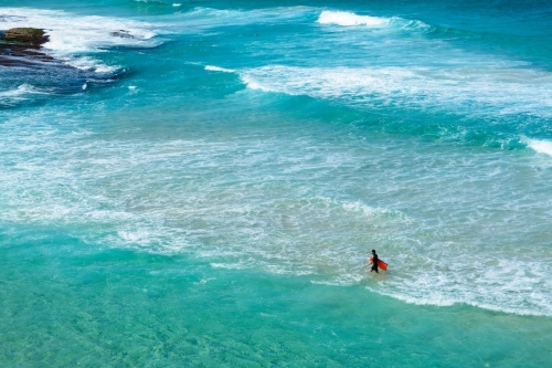 Boy walking in the water holding a body board at the beach - Australian Stock Image