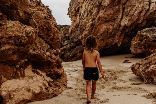 Boy walking through gap in rocks on beach - Australian Stock Image