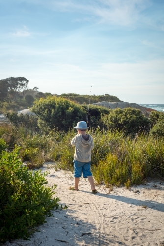 Boy walking with fishing rod on path to beach - Australian Stock Image