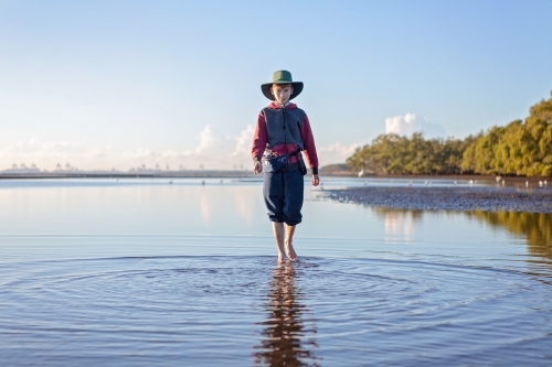 Boy walks on the beach at lowtide in winter barefoot - Australian Stock Image