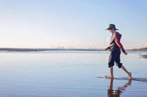 Boy walks on the beach at lowtide in winter barefoot - Australian Stock Image