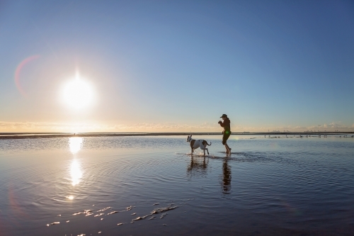 Boy walks on the beach at lowtide in winter barefoot with his dog