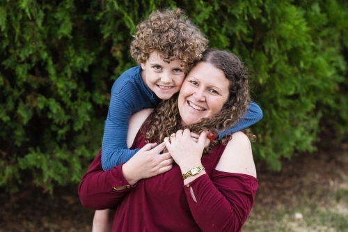 Boy with arms around mother sitting outside - Australian Stock Image