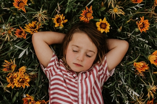 Boy with eyes closed laying in bed of flowers - Australian Stock Image