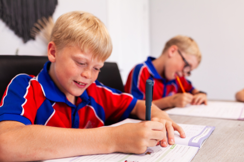 Boy working on homework bookwork with siblings after school at home - Australian Stock Image