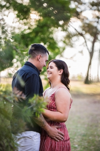 Boyfriend and girlfriend standing together behind tree looking and smiling at each other