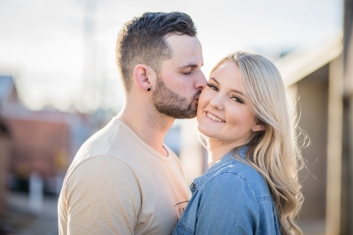 Boyfriend kissing smiling girlfriend on cheek - Australian Stock Image
