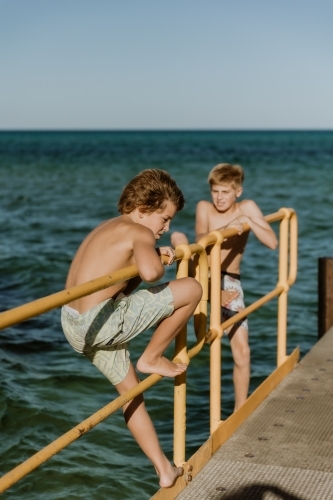 Boys climbing on Jetty by the sea - Australian Stock Image