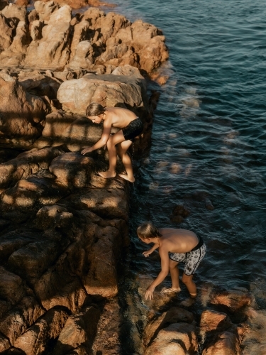 boys climbing rocks by the seaside - Australian Stock Image
