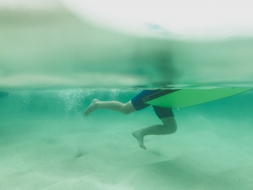 Boys legs underwater pushing off ground holding onto body board - Australian Stock Image