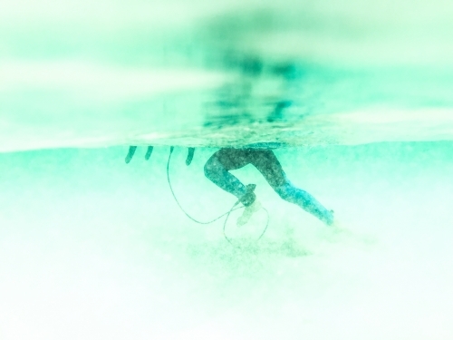 Boys legs underwater pushing surfboard