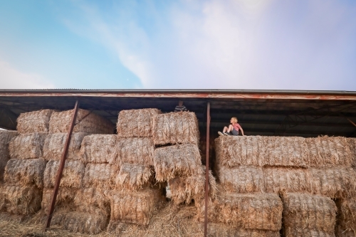 Boys sitting on top of hay bales in shed. Play time on the farm. - Australian Stock Image