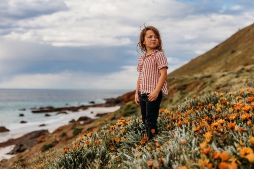 Boys standing on hill of flowers next to the ocean and rocks - Australian Stock Image