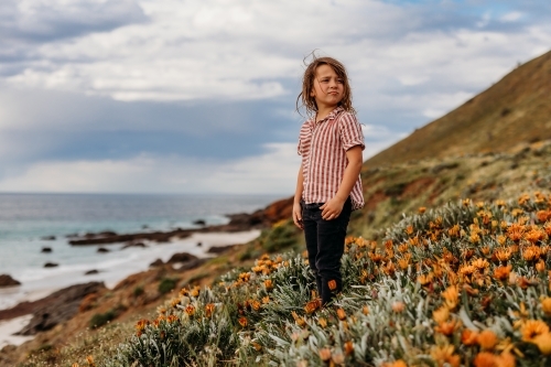Boys standing on hill of flowers next to the ocean and rocks