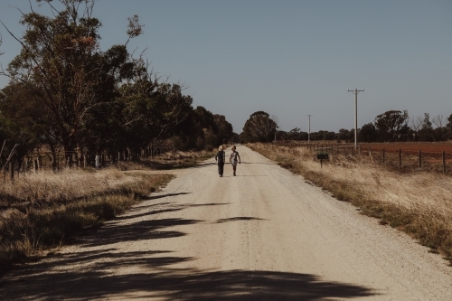 Boys walking along remote country road surrounded by fields - Australian Stock Image