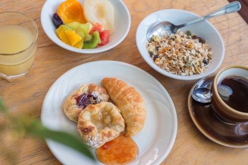 Breakfast food spread of pastries cereal fruit juice and coffee on table - Australian Stock Image