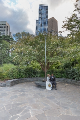 Bride and groom sitting together in city park - Australian Stock Image