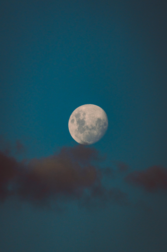 Bright waxing gibbous moon rising above soft evening clouds - Australian Stock Image