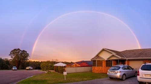 Brightly coloured rainbow curtain over houses at dusk - home concept - Australian Stock Image