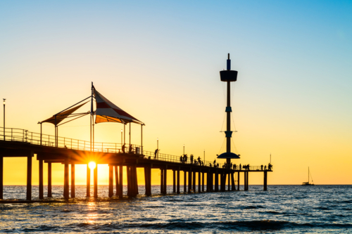 Brighton Jetty with people silhouettes viewed from the beach while the sun goes behind the horizon - Australian Stock Image