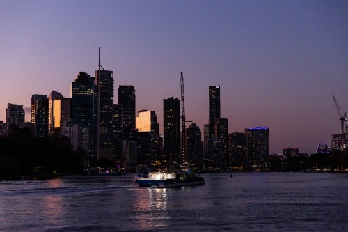 Brisbane city skyscrapers and ferry after sunset